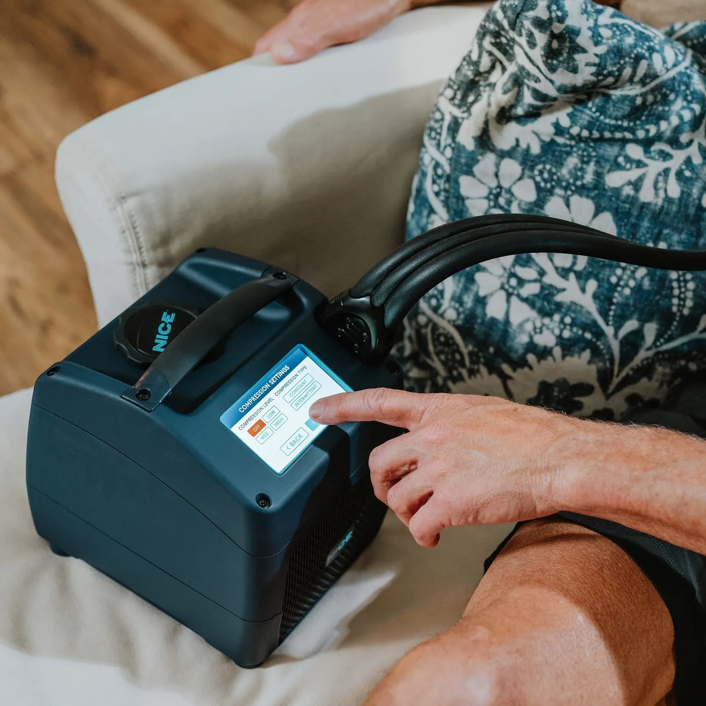 A person adjusting compression settings on the NICE1's touchscreen from a sofa at home